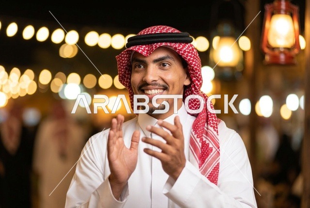 رجل سعودي مبتسم يرتدي الشماغ ويصفق في احتفال ليلي