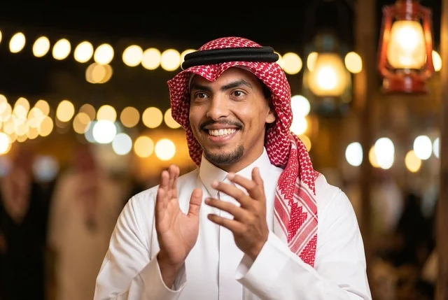 رجل سعودي مبتسم يرتدي الشماغ ويصفق في احتفال ليلي