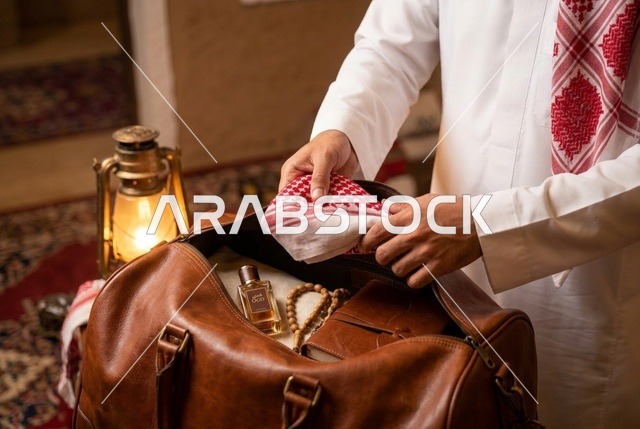 رجل سعودي يجهز حقيبة سفر جلدية مع الشماغ