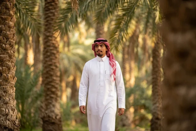 رجل سعودي يرتدي الثوب التقليدي ويمشي في مزرعة نخيل
