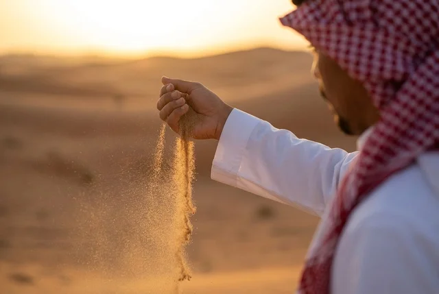 رجل سعودي يسكب رمال الصحراء الذهبية وقت الغروب