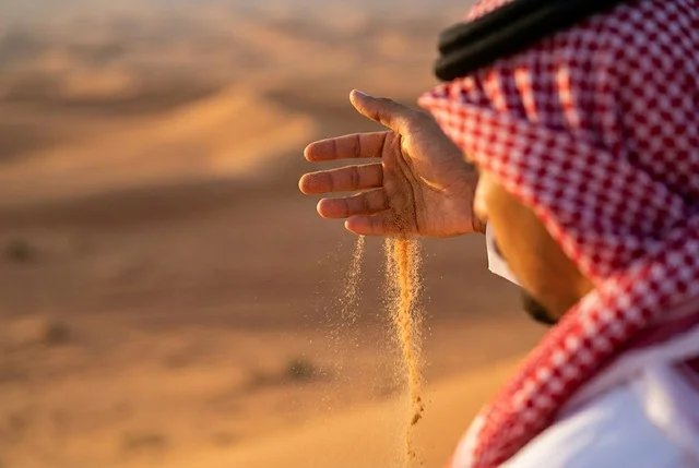 رجل سعودي يمسك بالرمال في الصحراء وقت الغروب