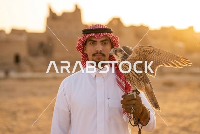 رجل سعودي يحمل صقراً وسط الأنقاض التراثية وقت الغروب