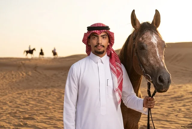 رجل سعودي مع خيل عربي في الصحراء وقت الغروب