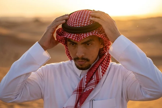 رجل سعودي يرتدي الشماغ التقليدي في الصحراء وقت الغروب