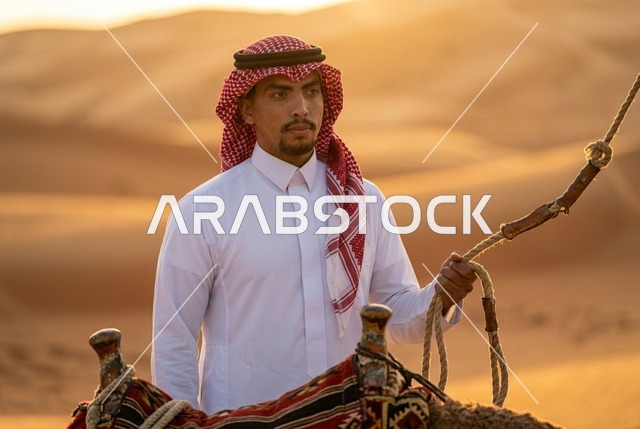 رجل سعودي بالزي التقليدي مع جمل في الصحراء عند الغروب