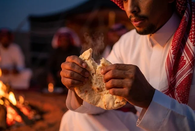 رجل سعودي يقطع الخبز الساخن بجانب شبة النار ليلاً