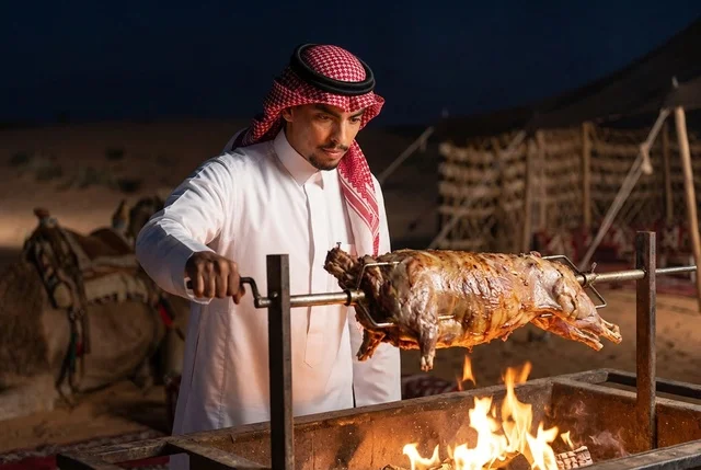 رجل سعودي يشوي خروف كامل على النار في مخيم صحراوي ليلاً