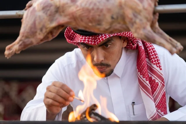 رجل سعودي بالزي التقليدي يشعل النار لشواء خروف كامل