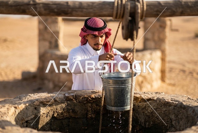رجل سعودي يسحب دلو الماء من بئر صحراوي قديم