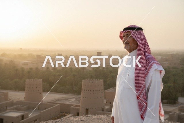 رجل سعودي يرتدي الزي التقليدي في قرية طينية تاريخية وقت الغروب