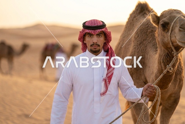 رجل سعودي يرتدي الزي التقليدي يقود جملا في الصحراء
