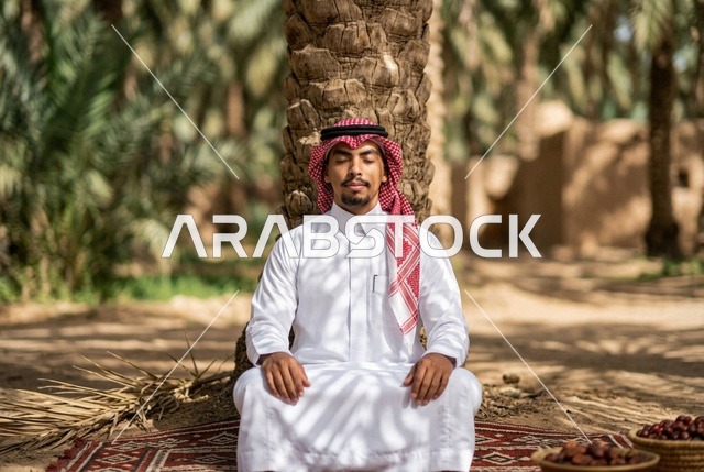 رجل سعودي يتأمل تحت نخلة في واحة تراثية