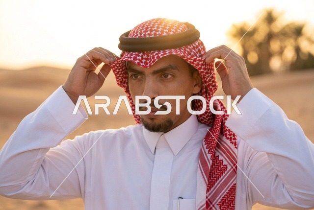 رجل سعودي بالزي التقليدي يعدل الشماغ في غروب الصحراء