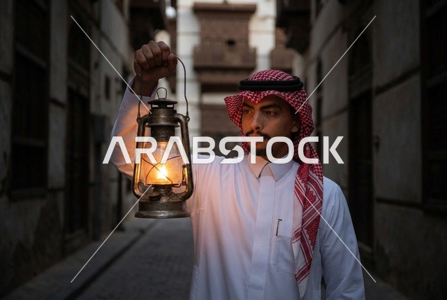 رجل سعودي يحمل فانوساً مضيئاً في زقاق تاريخي ليلاً