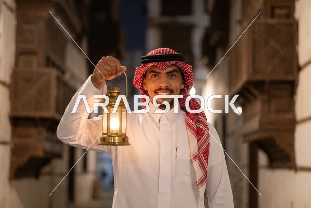 رجل سعودي يحمل فانوس رمضان مضيء في شارع تراثي