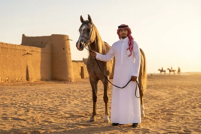 رجل سعودي مع حصان عربي في الصحراء التراثية وقت الغروب