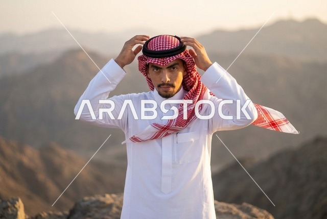 شاب سعودي بالثوب والشماغ على قمة جبل وقت الغروب