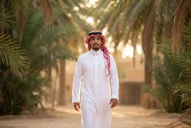 شاب سعودي بالزي التقليدي يمشي في واحة النخيل الدافئة