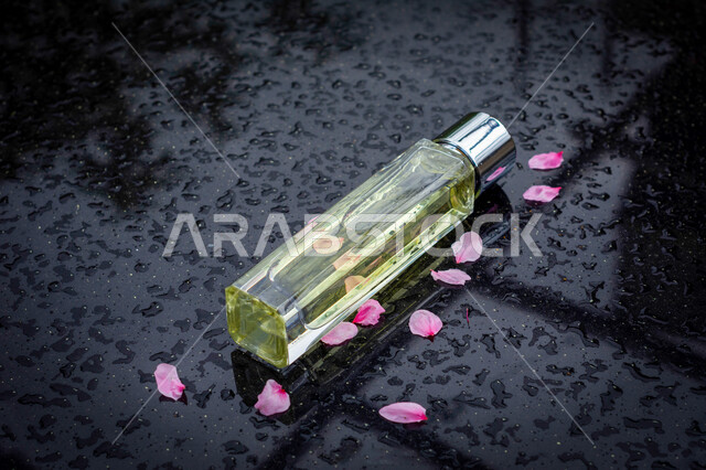 صورة إبداعية لزجاجة عطر متناثر حولها ورق الورد تحت قطرات المطر، التعطر والتطيب، فن تصوير المنتجات والعطور، قطرات المطر، عطور خليجية سعودية