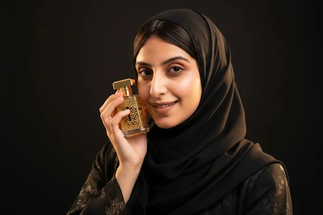 امرأة عربية بالحجاب الأسود تحمل زجاجة عطر ذهبية فاخرة