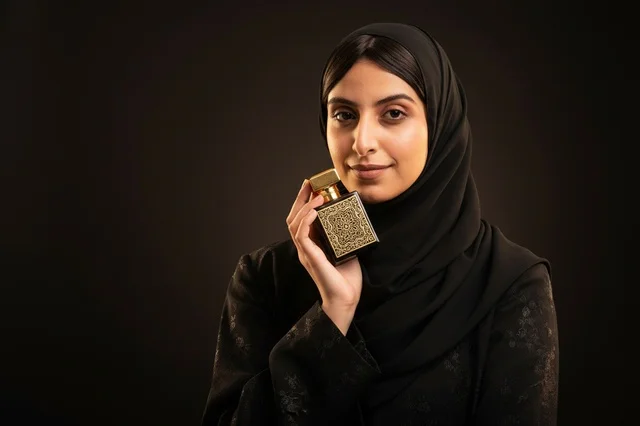 امرأة عربية تحمل زجاجة عطر فاخرة في الاستوديو