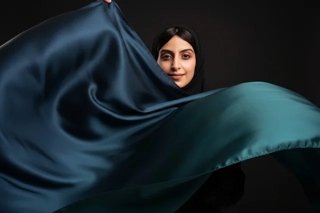 امرأة عربية تحمل قماش ستان أخضر متموج في الاستوديو امرأة عربية تحمل قماش ستان أخضر متموج في الاستوديو
