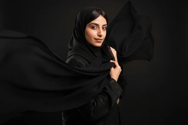 An Arab woman in a black abaya and hijab in the studio.