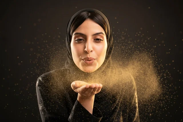 امرأة عربية بالعباءة والحجاب تنفخ الغبار الذهبي
