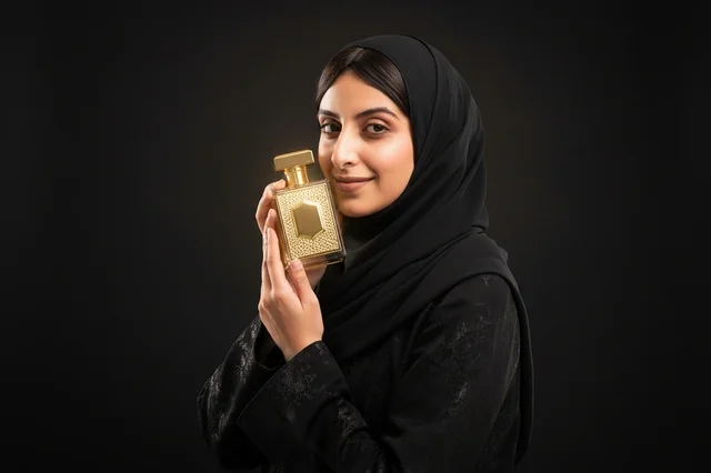امرأة عربية بالعباءة تحمل زجاجة عطر ذهبية فاخرة