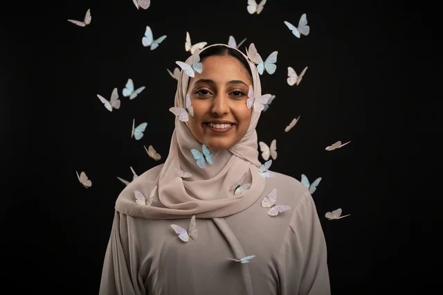 امرأة عربية محجبة مبتسمة مع فراشات على خلفية سوداء