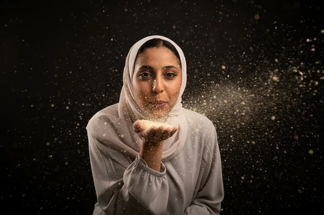 An Arab woman wearing a hijab is blowing a shiny sparkle in the studio.