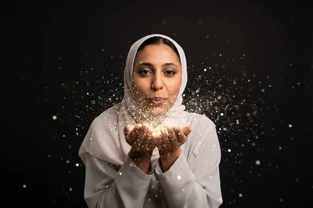 امرأة عربية بالحجاب تنفخ بريقاً ذهبياً بخلفية سوداء