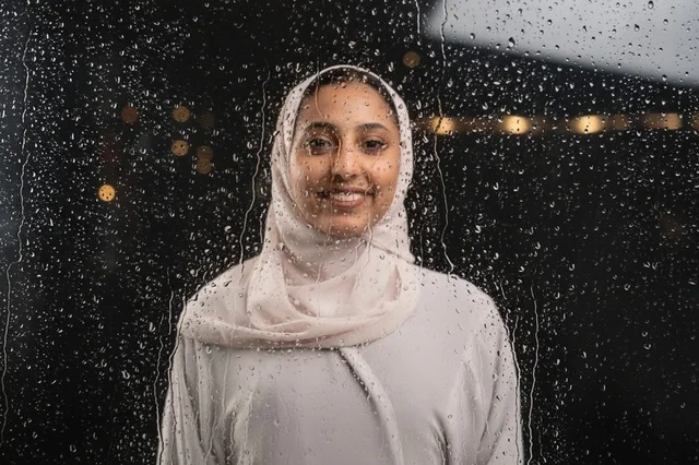 امرأة عربية بالحجاب الأبيض خلف نافذة زجاجية ممطرة ليلا