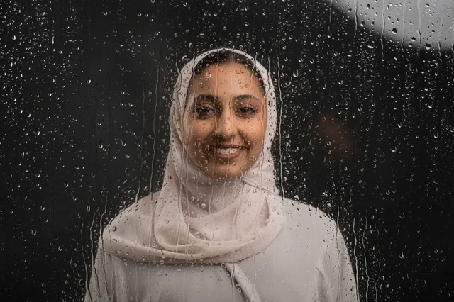 امرأة عربية بالحجاب الأبيض خلف نافذة زجاجية ممطرة