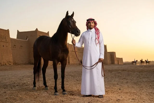 رجل سعودي مع حصان عربي عند قلعة تراثية وقت الغروب