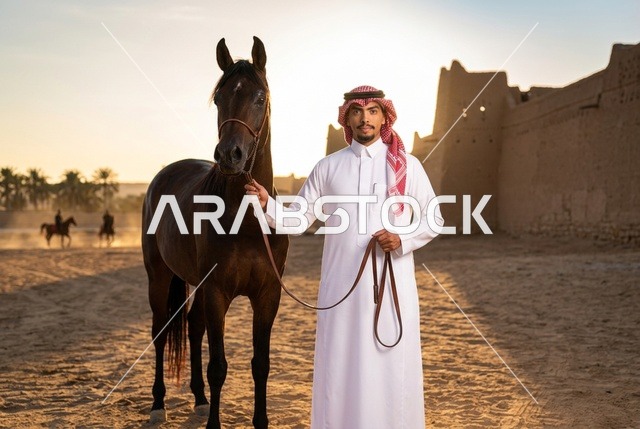 رجل سعودي مع حصان عربي عند قلعة تراثية وقت الغروب