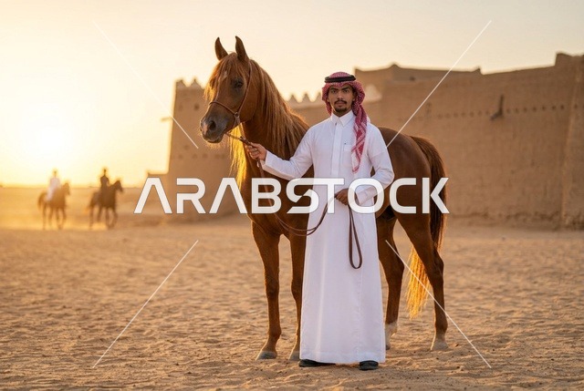 رجل سعودي مع حصان عربي عند قلعة تراثية وقت الغروب