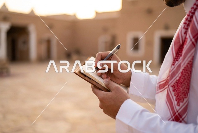رجل سعودي يكتب في دفتر ملاحظات بموقع تراثي
