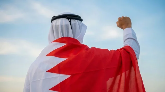 رجل بحريني ملتف بعلم البحرين ويرفع قبضة يده في السماء