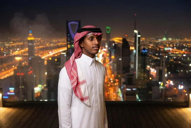 رجل سعودي بالزي التقليدي مع أفق مدينة الرياض ليلاً