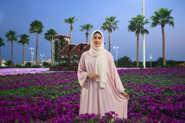 امرأة عربية بالعباءة الوردية في حديقة زهور بنفسجية