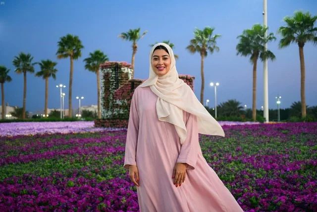 امرأة عربية بعباءة وردية في حديقة زهور بنفسجية