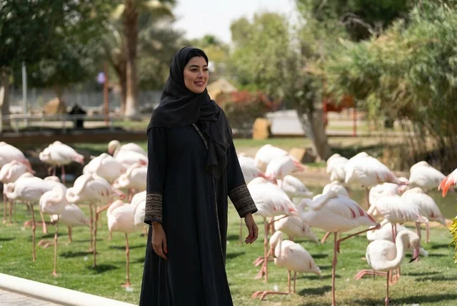 امرأة عربية بالعباءة تمشي مع الفلامنجو في الحديقة