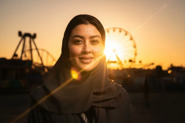 امرأة عربية بالحجاب في مدينة الملاهي عند غروب الشمس