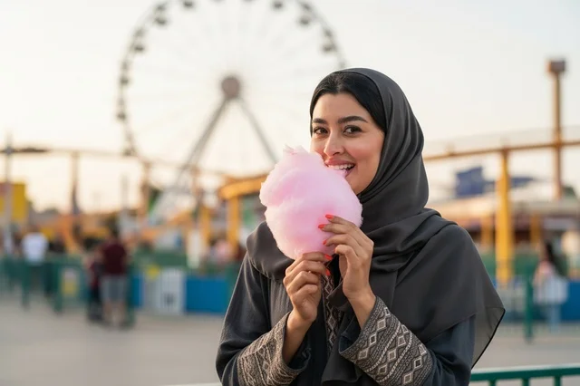امرأة عربية مبتسمة تحمل غزل البنات في مدينة الملاهي