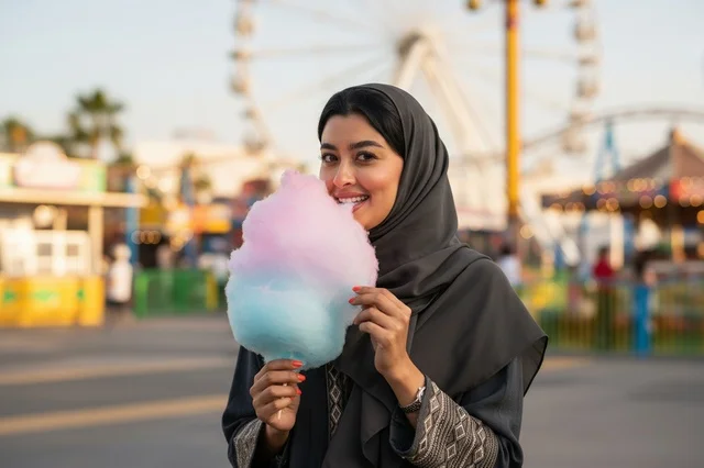 امرأة سعودية مبتسمة مع حلوى غزل البنات في الملاهي