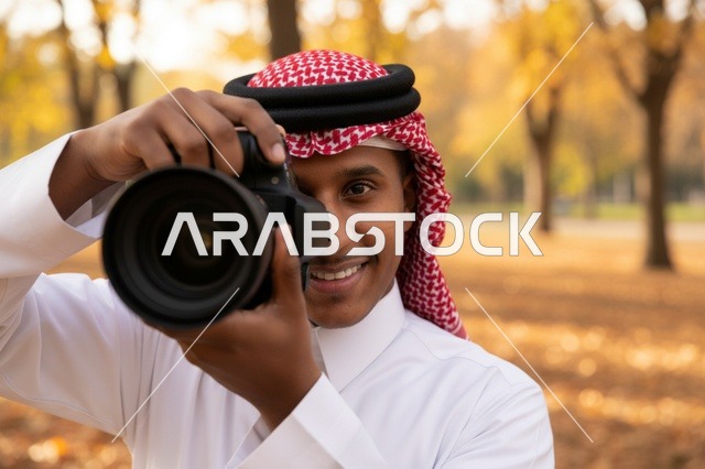 مصور سعودي بالزي التقليدي يحمل كاميرا في حديقة خريفية