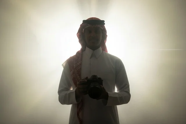 مصور سعودي يحمل كاميرا احترافية مع إضاءة خلفية ضبابية