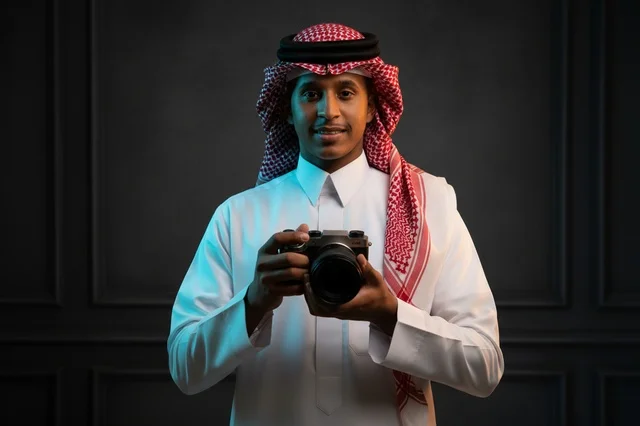 مصور سعودي يرتدي الزي التقليدي يحمل كاميرا في الاستوديو
